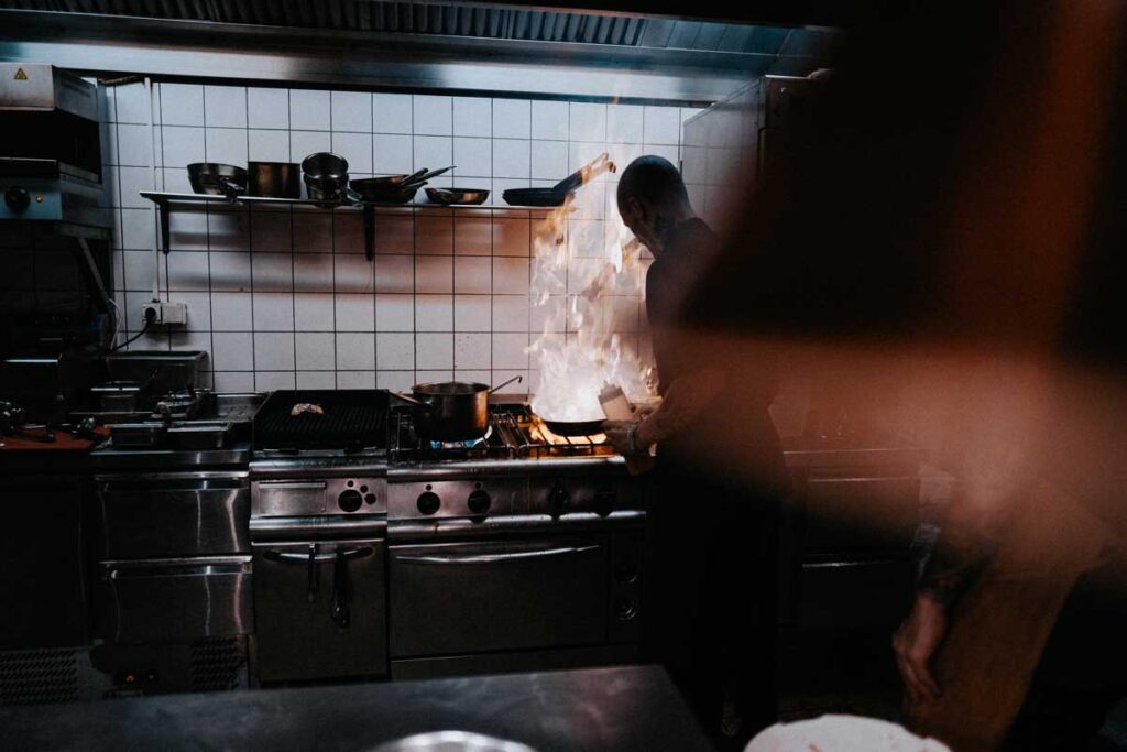 chef in restaurant kitchen with large flames coming from pan
